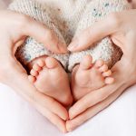 Baby feet in mother hands. Tiny Newborn Baby's feet on female Heart Shaped hands closeup. Mom and her Child. Happy Family concept. Beautiful conceptual image of Maternity